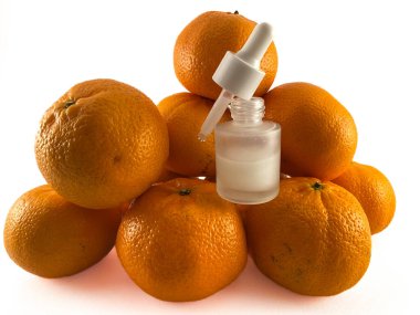 Portakal yığını üzerine bir şişe portakal renkli sıvı serum yakın plan. Şişenin bir damlası ve parlak gümüş bir kapağı var. Kozmetik veya cilt bakımı için kullanılabilir.. 