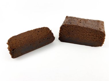 Beyaz arka planda izole edilmiş iki parça çikolatalı kek ya da browni. Pasta dilimlerinin ortasında kalın bir çikolata tabakası var ve üzeri pudra şekeriyle kaplanmış..