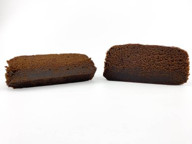 Beyaz arka planda izole edilmiş iki parça çikolatalı kek ya da browni. Pasta dilimlerinin ortasında kalın bir çikolata tabakası var ve üzeri pudra şekeriyle kaplanmış..