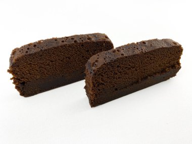 Beyaz arka planda izole edilmiş iki parça çikolatalı kek ya da browni. Pasta dilimlerinin ortasında kalın bir çikolata tabakası var ve üzeri pudra şekeriyle kaplanmış..
