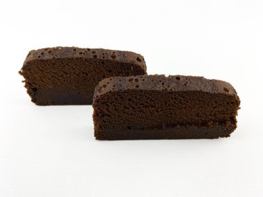 Beyaz arka planda izole edilmiş iki parça çikolatalı kek ya da browni. Pasta dilimlerinin ortasında kalın bir çikolata tabakası var ve üzeri pudra şekeriyle kaplanmış..