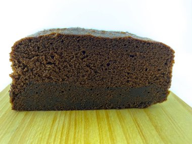 Tahta bir tahtanın üzerinde taze pişmiş çikolatalı pasta. Pasta, zengin, koyu kahverengi bir renk ve hafif desenli hava cepli bir bluza sahip. Nemli ve yoğun görünüyor, lezzetli bir hoşgörüyü davet ediyor.