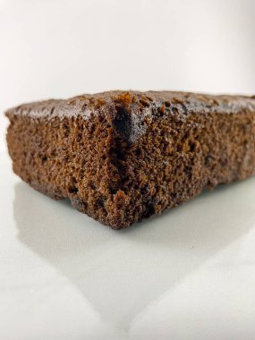 Yansıması olan beyaz bir tabakta browninin yakın çekimi. Browni kare şeklindedir ve kıvrımlı bir dokusu vardır. Gıda geçmişi ya da el ilanları için kullanılabilir.