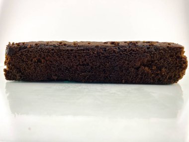 Bir dilim çikolatalı kek ya da tüm browni beyaz bir tabakta yansımalı duruyor. Pasta kahverengi ve üzerinde pürüzsüz bir doku var. düz çekim