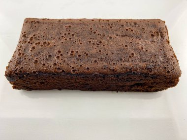 Bir dilim çikolatalı kek ya da tüm browni beyaz bir tabakta yansımalı duruyor. Pasta kahverengi ve üzerinde pürüzsüz bir doku var. düz çekim