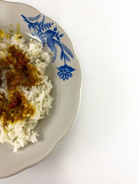 Pilav ve körili tavukla birlikte beyaz bir tabağın yakın çekimi. Körili tavuk koyu kahverengi renktedir ve koparılmış ya da doğranmış gibi görünür. Düz yatıyordu.