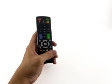 Uzaktan kumandayı tutan bir el. Kumanda siyah ve üzerinde bir sürü düğme var. Uzaktan kumandayı avucunun içinde tutan kişinin başparmağı OK tuşuna basıyor.