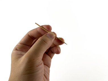 Kürdan tutan bir el. Kürdan ahşaptan yapılmıştır ve bir ucu keskindir. El, kürdanı başparmak ve işaret parmağı arasında tutuyor. Arkaplan beyaz.