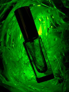 Su damlalarında yeşil bir parfüm şişesi. Parfüm neon yeşili. Arka plan, mesaj için yer. Erkek parfümü. Kadın parfümü.. 