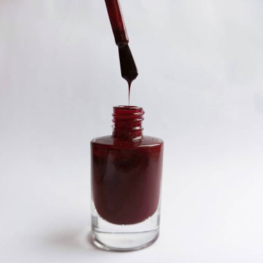 Açık bir oje kavanozu. Beyaz arka planda Burgundy tırnak cilası. Kırmızı oje damlaları fırçadan kavanoza akıyor. Metin için bir yer. 