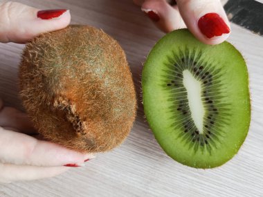 Bir kadın kivi tutuyor. Koca bir kivi ve bölünmüş kivi. Kivinin faydaları ve zararları. Yiyeceklerde C vitamini. Geçmişi. Bir dilim kiwifruit..