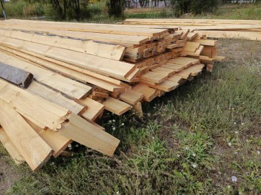 İnşaat için tahta kirişler. İnşaat tahtaları üst üste istiflenir ve yerde yatar. İnşaat alanı. Bıçkıhane. Arkaplan.