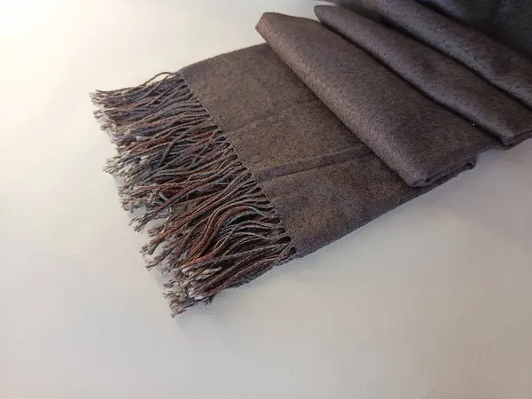 Beyaz arka planda püsküllü gri eşarp. Fular masanın üzerinde katlanmış akordeon. Soğuk kış ve sonbahar havası için sıcak giysi aksesuarı. Arkaplan.