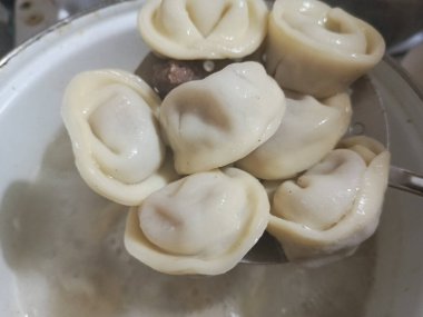 Pelmeni bir tencerede kaynatılır. Yuvarlak bir kaşık, pişmiş pelmeni 'yi kaynar sudan çıkarır. Ev yapımı pelmeni pişiriyorum. Geçmişi. Doğal fotoğraf. Pelmeni bir kaşıkta.