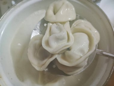 Pelmeni kaynamış bir kaşıkla kaynar suyla bir tencereden çıkarılır. Et ile ev yapımı pelmeni pişirmek. Reklam için arka plan, mesaj için alan. Doğal fotoğraf. Pelmeni bir kaşıkta.