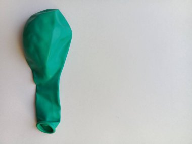 Yeşil bir balon. Beyaz bir masada sönmüş bir balon. Çocuklar için oyuncaklar. Metin için arkaplan, boşluk.