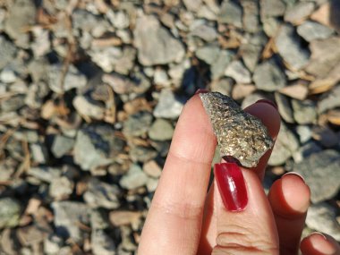 Bir kadının eli parlak altın benekli bir taşı tutar. Parlak taş güneşte parıldıyor. Kıyıda çakıl taşları. Reklam için arka plan, metin için yer. 