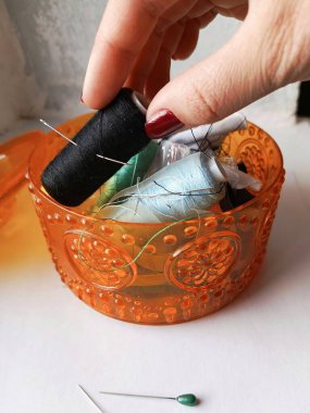 Bir terzinin eli bir kutudan bir makara siyah iplik alır. Dikiş dikmek için iğne ve ipliklerle dolu bir kutu. Giysi tamiri. Arkaplan.