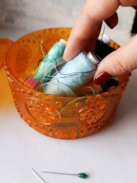 Bir kadının eli, iplik ve iğnelerle dolu bir kutudan bir makara mavi iplik alır. Dikiş dikme ve giysi tamir konsepti. Metin için arkaplan, boşluk.