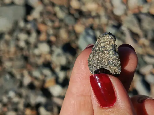 Bir kadının eli parlak altın benekli bir taşı tutar. Parlak taş güneşte parıldıyor. Kıyıda çakıl taşları. Reklam için arka plan, metin için yer. 