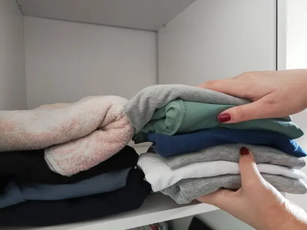 Kadınların elleri katlanmış şeyleri dolabın rafına koyuyor. Evi temizliyorum. Giysileri dolapta saklıyorum. Arka plan, mesaj için yer. Elinde bir yığın kıyafet vardı..