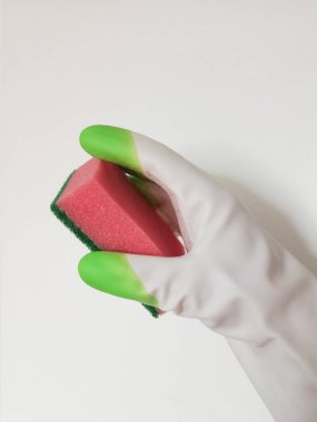 Plastik eldivenli bir el beyaz arka planda bulaşık yıkamak için kırmızı bir sünger tutar. Daireyi temizliyorum. Temizlik. Arkaplan.