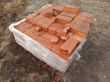 Yerde bir paket kırmızı tuğla duruyor. Duvarlar için inşaat malzemeleri. Arkaplan.