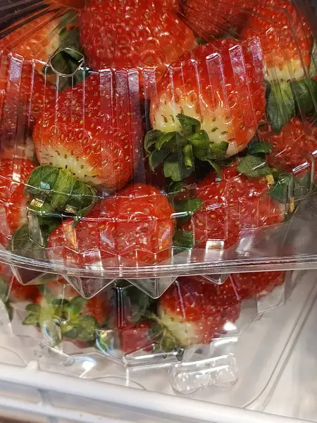 Süpermarketin camındaki plastik bir kutuda kırmızı, sulu çilekler. Reklam için arka plan, metin için yer. Taze çilek satışı. 