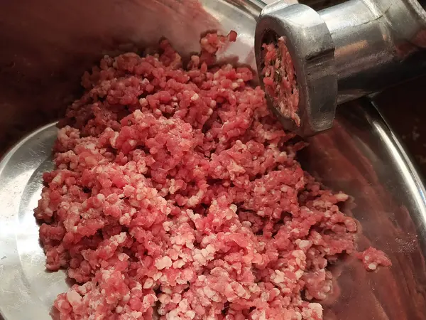 Eski bir kıyma makinesi et öğütür. Metal bardakta çiğ et. Yakın plan. Arka plan, mesaj için yer. Kasap işi..