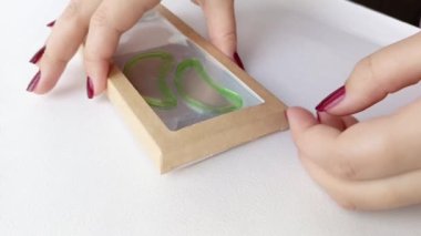 Karton bir hediye kutusunda, şeffaf bir pencereyle el yaması yapıştırıyor. Teslimat konsepti için ürün paketleme. Video.