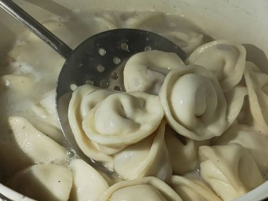 Etli börekler yakın plan bir tencerede kaynar suda pişirilir. Arka plan, mesaj için yer. Yarı pişmiş pelmeni pişirme.