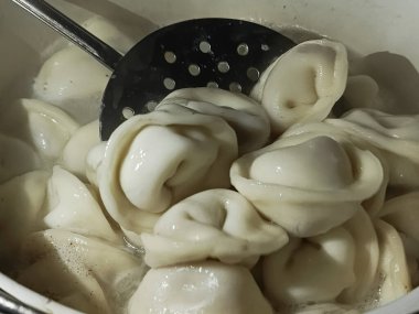 Etli börekler yakın plan bir tencerede kaynar suda pişirilir. Arka plan, mesaj için yer. Yarı pişmiş pelmeni pişirme.