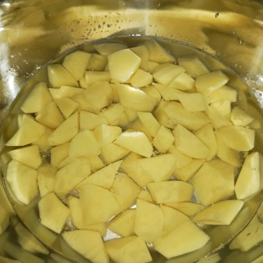 Metal bir bardakta suyla patates doğradım. Nişastandan çiğ patates. Sebze soyuyordum. Çorba konsepti. Geçmişi. Tabakta patates dilimleri.
