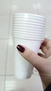Bir kadının elinde tek kullanımlık plastik bardaklar var. Beyaz su bardakları.