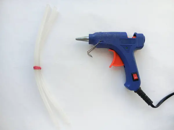 Sıcak tutkal tabancası ve çubuklar beyaz bir masada. Çeşitli nesneleri yapıştırmak için mavi sıcak yapıştırıcı, karton.