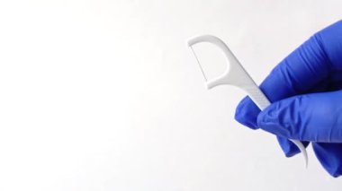 Beyaz arka planda plastik saplı diş ipi. Mavi tıbbi eldivenli dişçinin eli diş ipini yakından tutuyor. Diş temizliği için dişçinin tavsiyesi.