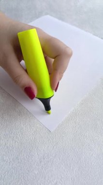 Bir kadının eli, üzerinde sarı kalem olan bir kağıt parçasının altını çizer. Soyut. Kadın tükenmez kalemle yazıyor..