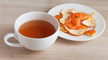 Mandalina kabuklu çay. Bir kupa sıcak çay ve masanın üzerinde mandalina kabuğu olan bir tabak. Soğuk algınlığı için sıcak içecek.. 