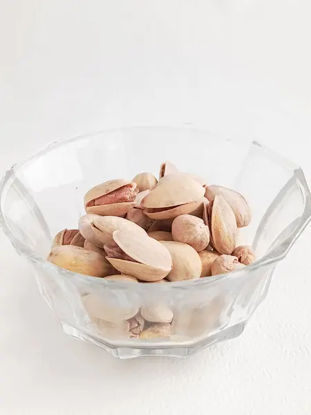 Beyaz arka planda cam bardakta duran tuzlu şam fıstığı. Fındıkların faydaları. Sincaplar. Atıştırmalık Soyulmamış fıstıklar..