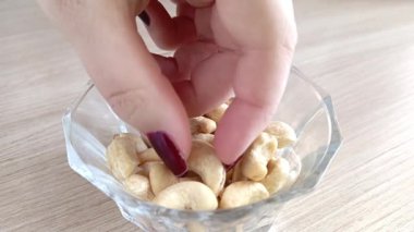 Bir kadının eli fındıktan fındık alır. Masanın üzerinde bir tabak kaju var. Sağlıklı bir atıştırmalık Fındıkların kalori içeriği.