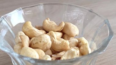Bir kadının eli fındıktan fındık alır. Masanın üzerinde bir tabak kaju var. Sağlıklı bir atıştırmalık Fındıkların kalori içeriği.
