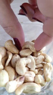 Bir kadının eli fındıktan fındık alır. Masanın üzerinde bir tabak kaju var. Sağlıklı bir atıştırmalık Fındıkların kalori içeriği.