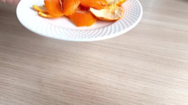 Bir kadın masanın üzerine mandalina kabuğu olan bir tabak koyar. Mandalina ve portakal kabuklarının faydaları. Turunçgil kabuklu çay..