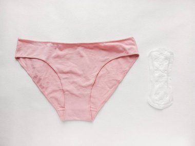 Masanın üzerinde kadın iç çamaşırı ve tek kullanımlık ped var. Tekrar kullanılabilir adet külotları ve tek kullanımlık pedleri karşılaştırın. Pedlere alerjim var. Hijyen ürünleri. Aylık döngü.