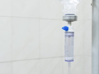 A hospital IV drip in close-up, with a place for text on the side. The infusion system on the background of tiles. Intravenous administration of drugs.  clipart