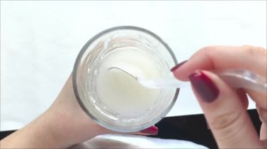 Bir kadın bir kaşıkla cam bardakta protein içeceği karıştırıyor. Kas kütlesi artıyor. Beslenme düzeninde protein.