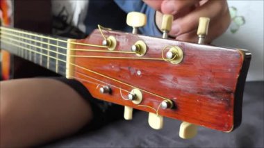 Genç bir çocuk kanepede oturuyor ve gitar tellerini ayarlıyor. Gitar dersi. Müzik aleti. Akortlar. 