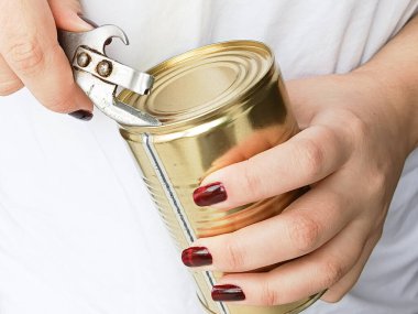 Beyaz tişörtlü bir kadın konserve açacağıyla teneke kutuyu açıyor. Kutuları açmak için bir bıçak. Konserve ürünler diyette.