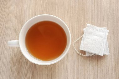 Mutfak masasında beyaz bir fincan sıcak çay ve iki poşet çay var. Siyah, yeşil çay poşetlerinin faydaları. Sabahları sıcak bir şeyler içerim..