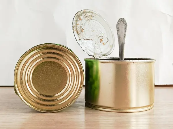 Bir teneke kutu ve tahta bir masanın üzerinde kaşık standı olan açık bir teneke kutu. Konserve balık, güveç, yeşil bezelye. Konserve yemek konservesi.